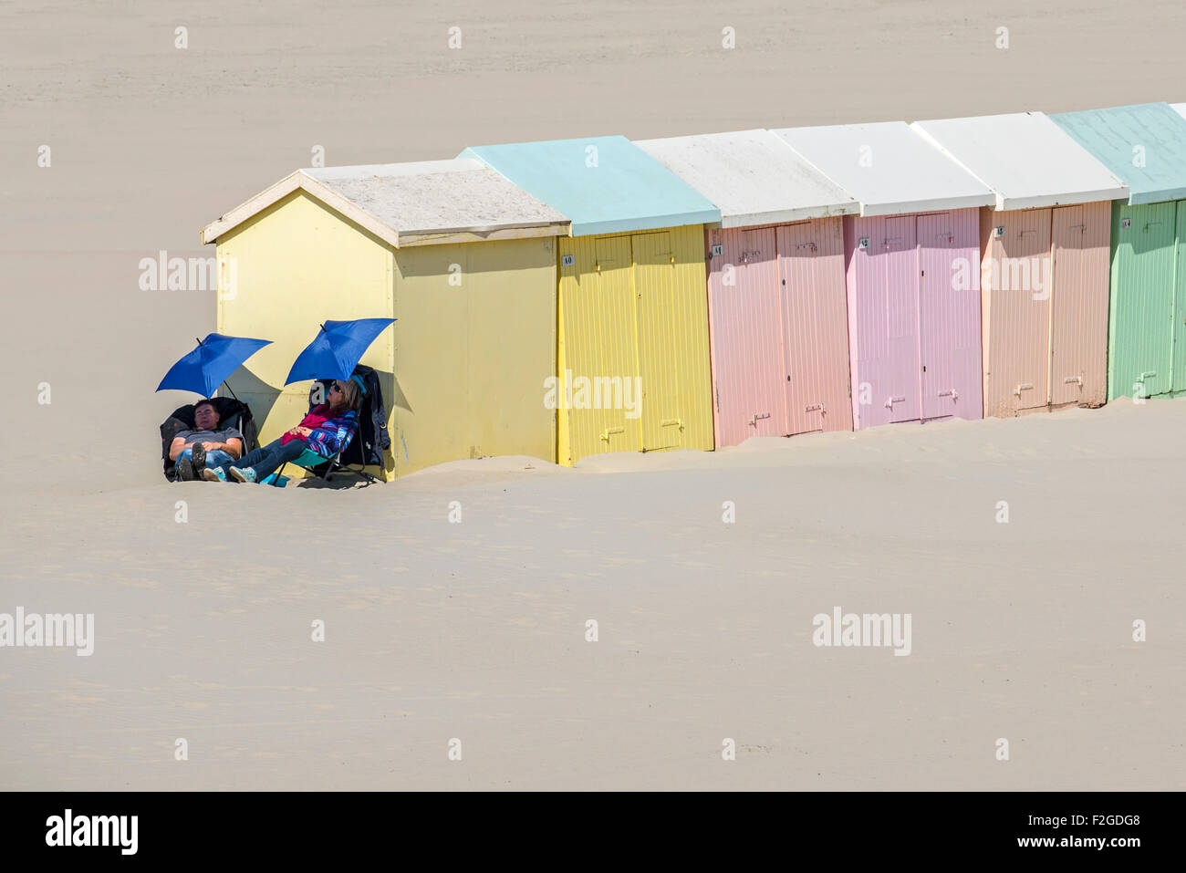 Deux excursionnistes endormi sous des parasols à côté de la plage de couleurs pastels cabines / abris, Berck / Berck-sur-Mer, Côte d'Opale, France Banque D'Images