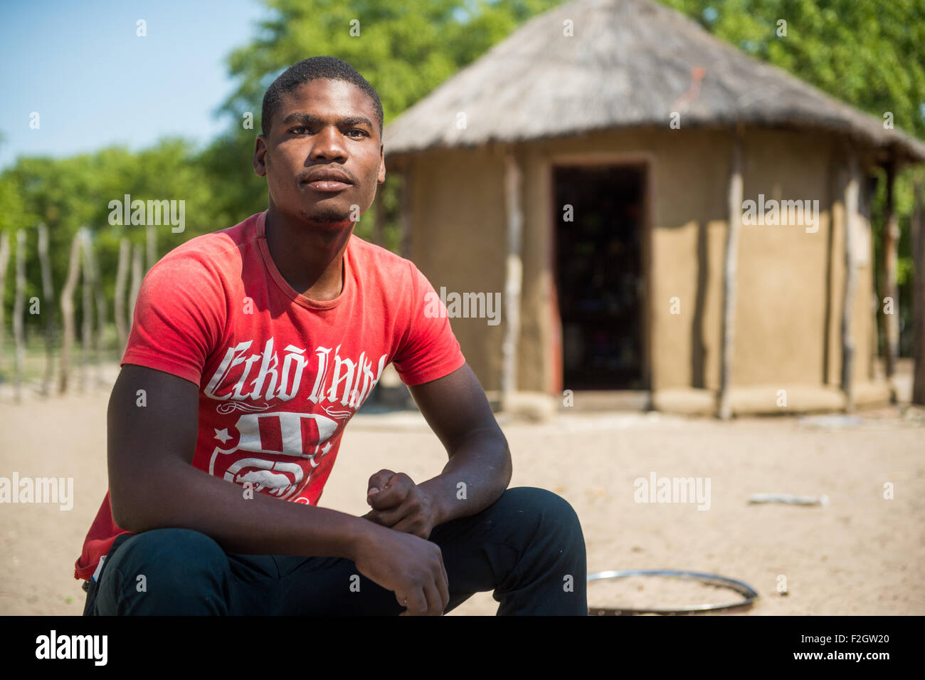 Homme africain assis en face de la hutte au toit de chaume au Botswana, l'Afrique Banque D'Images