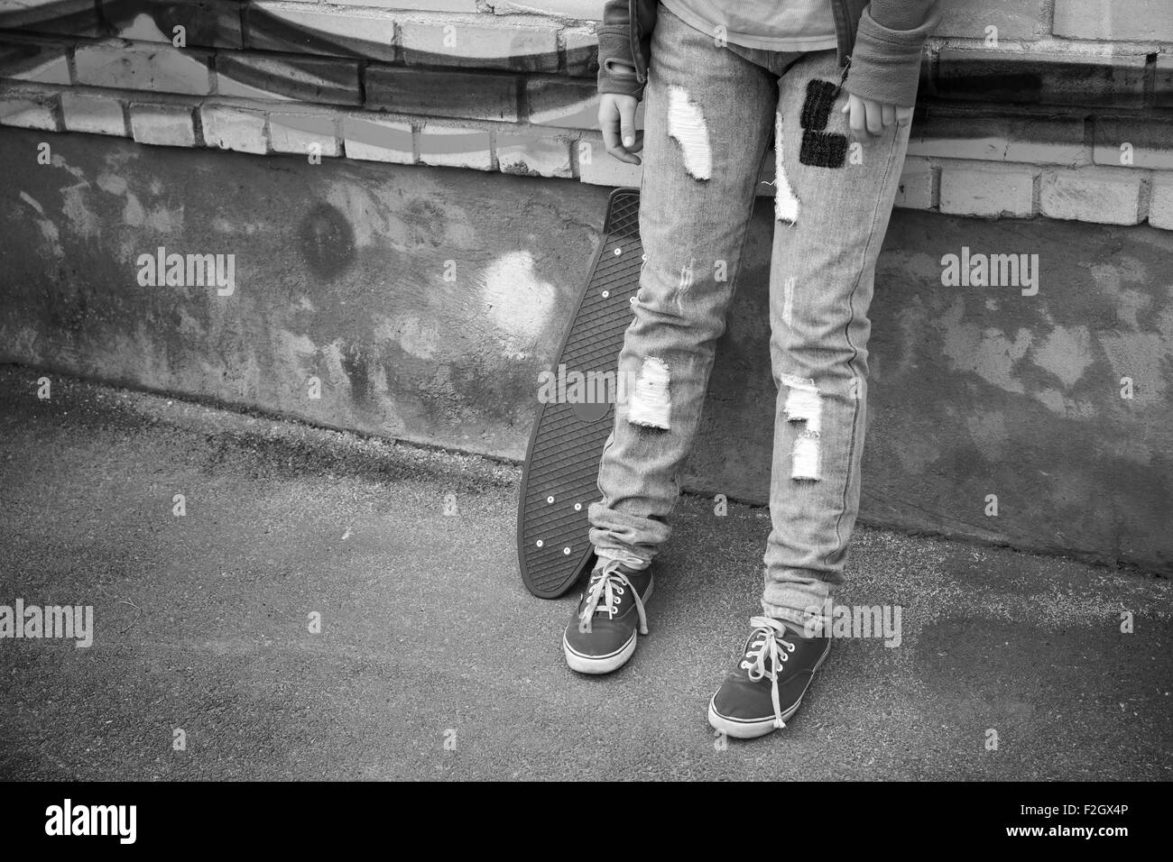 Adolescent en jeans et gumshoes stands avec skateboard près du vieux mur urbain Banque D'Images