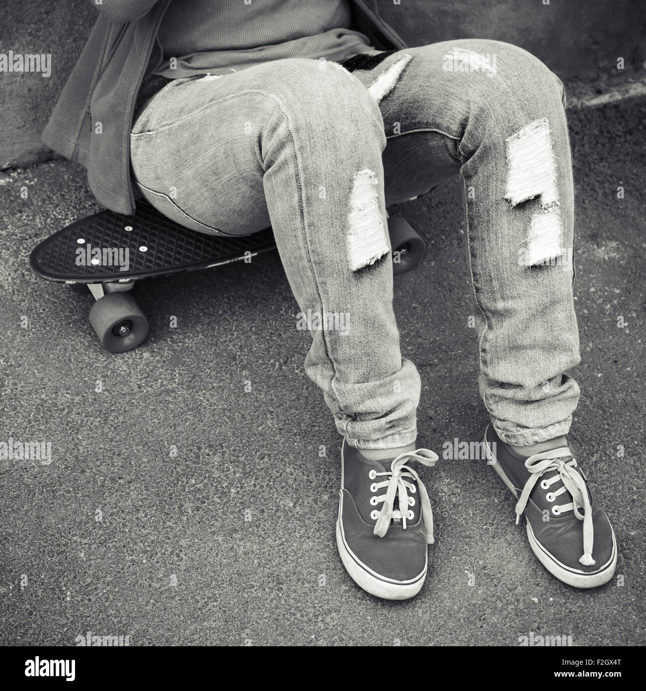 Adolescent en jeans et gumshoes est assis sur une planche à roulettes Banque D'Images