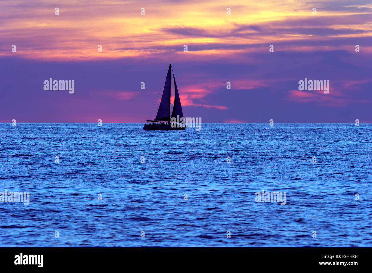 Voilier coucher du soleil est un bateau qui se profile et les personnes se déplaçant le long d'une mer bleue avec un ciel rempli de nuages colorés en arrière-plan. Banque D'Images