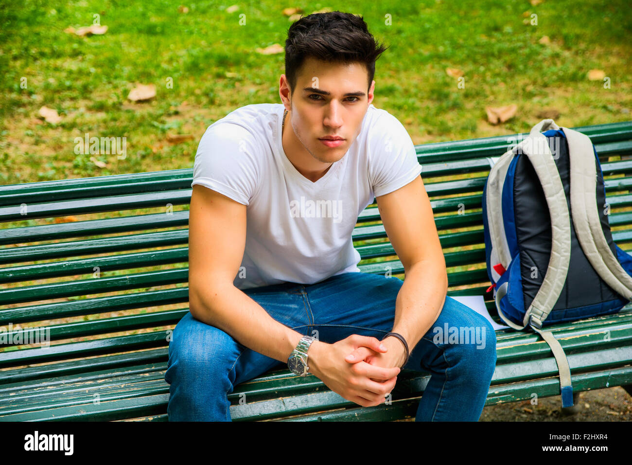 Jeune étudiant assis sur le banc dans un parc, à côté de son sac à dos, et tout en pensant à la suite au sérieux. Banque D'Images