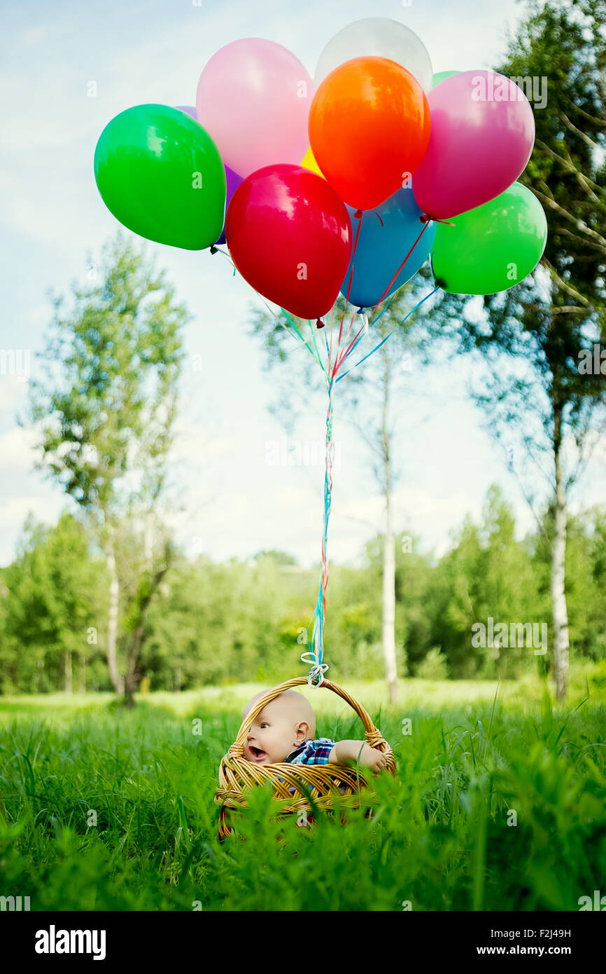 Un petit garçon est assis dans un panier avec des ballons colorés. Banque D'Images