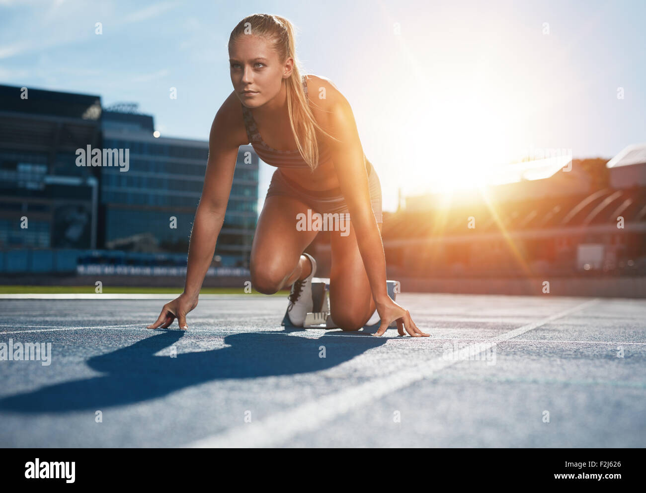 Mettre en place et en confiance femme en position de départ prêt pour la course. Athlète féminin sur le point de commencer un sprint à la route. Sunl lumineux Banque D'Images
