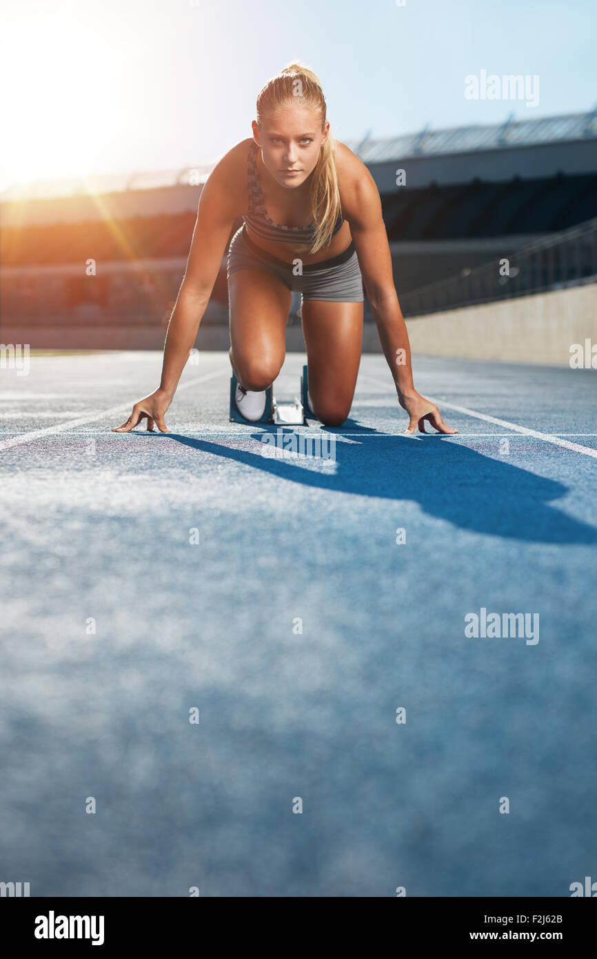 Jeune femme sprinter dans la position de démarrage sur une piste de course à un stade à la recherche jusqu'à l'appareil photo avec détermination. Runner Banque D'Images