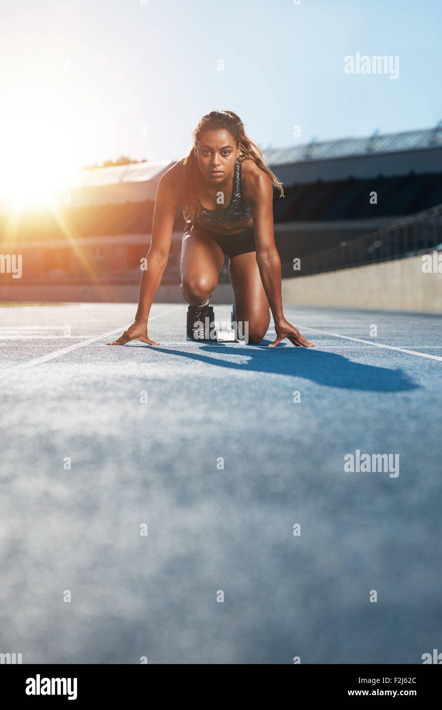 Shot verticale de jeunes femmes sprinter en tenant prêt à démarrer face à la caméra. Femme athlète en blocs de départ avec Banque D'Images