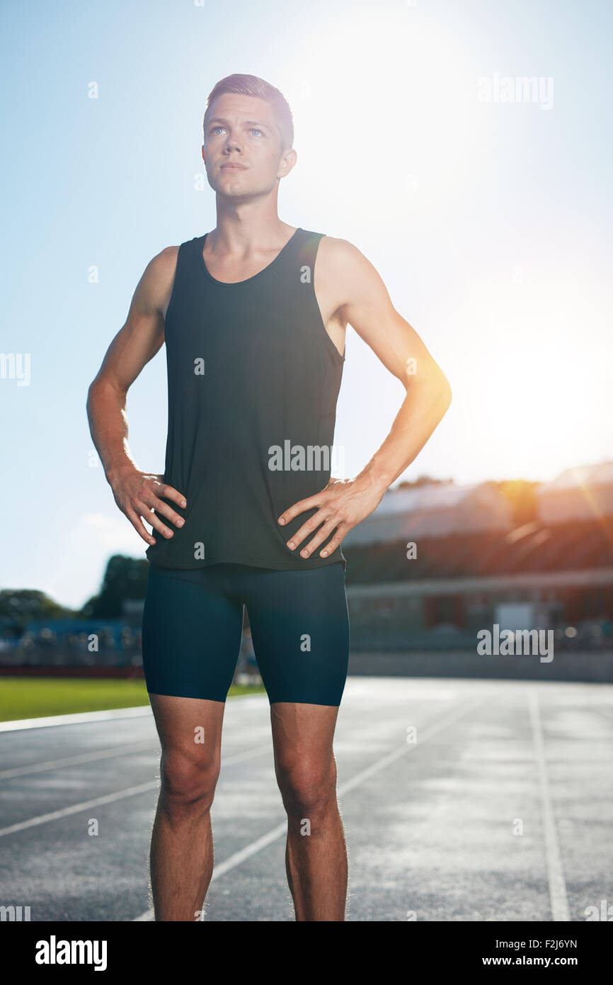 Fit young man standing avec ses mains sur les hanches à la route. La préparation de l'athlète masculin déterminé pour une course sur stade de l'athlétisme rac Banque D'Images