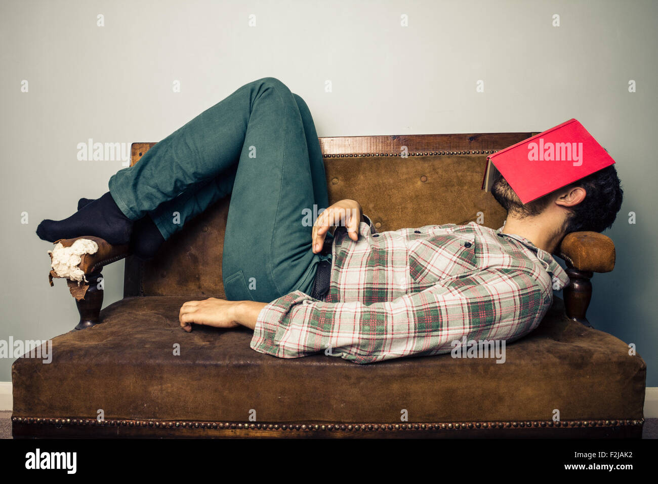 Jeune homme de dormir sur un canapé avec livre couvrant son visage Banque D'Images