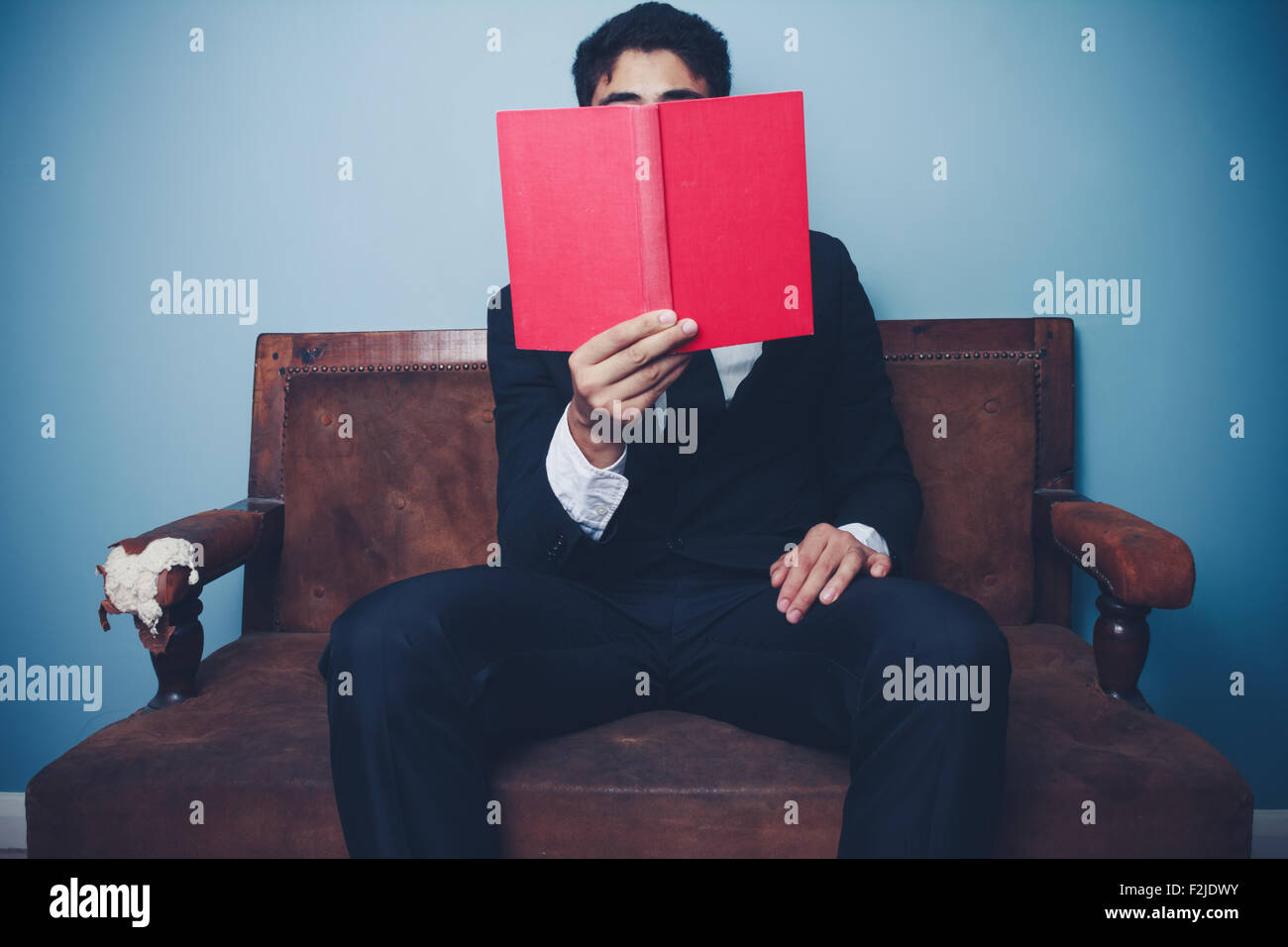 Young businessman sitting on sofa et la lecture d'un livre Banque D'Images