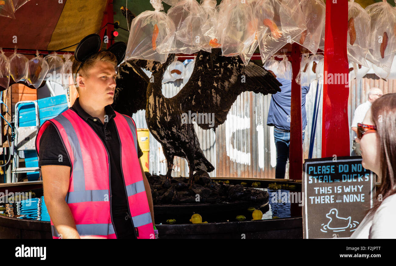 Un membre du personnel gai accueille un client pour le crochet d'un canard à l'Dismaland Banksy, où l'on peut gagner un poisson rouge mort dans un sac Banque D'Images