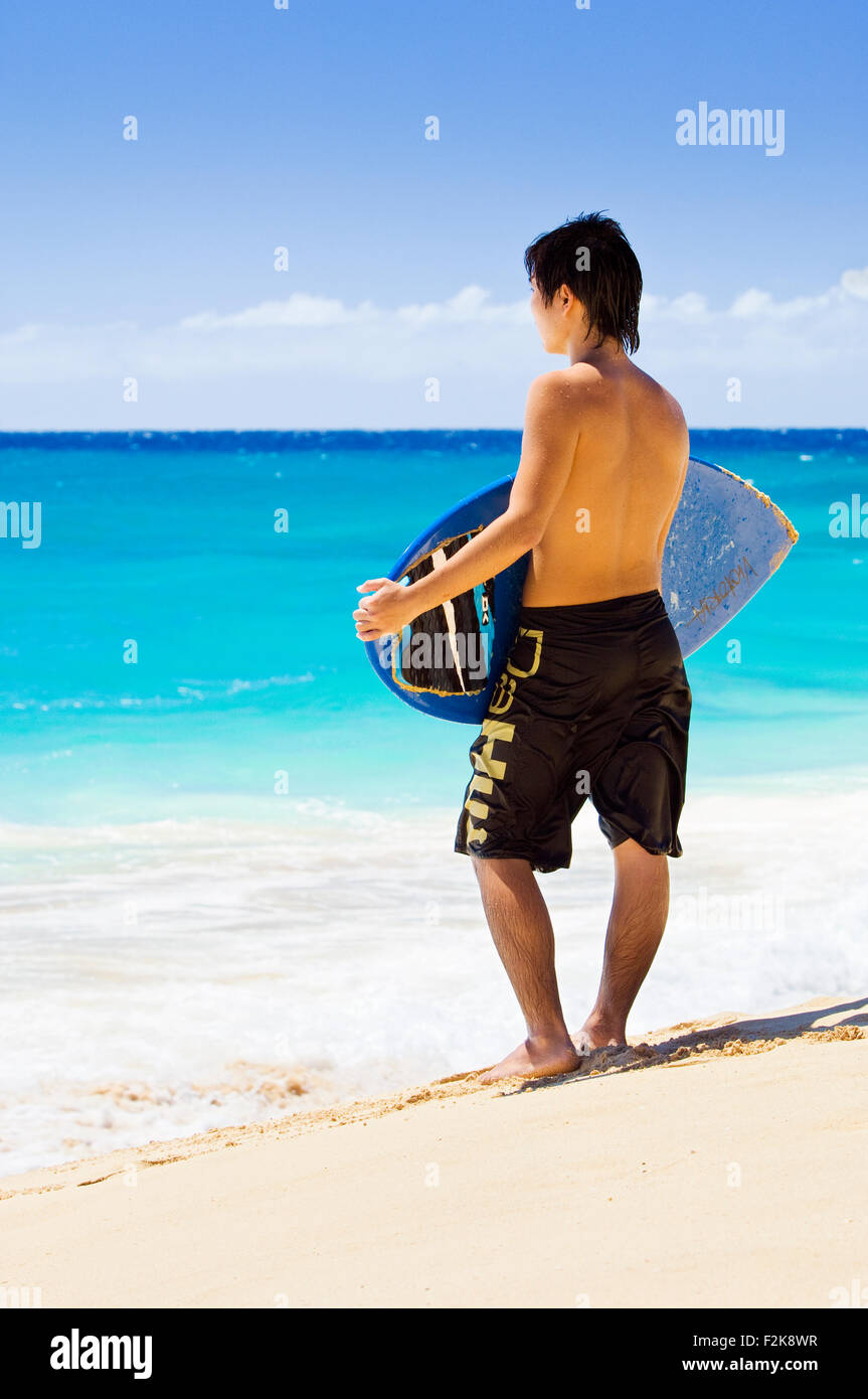 Boarder écrémé debout sur une plage de sable fin à Oahu, Hawaii Banque D'Images