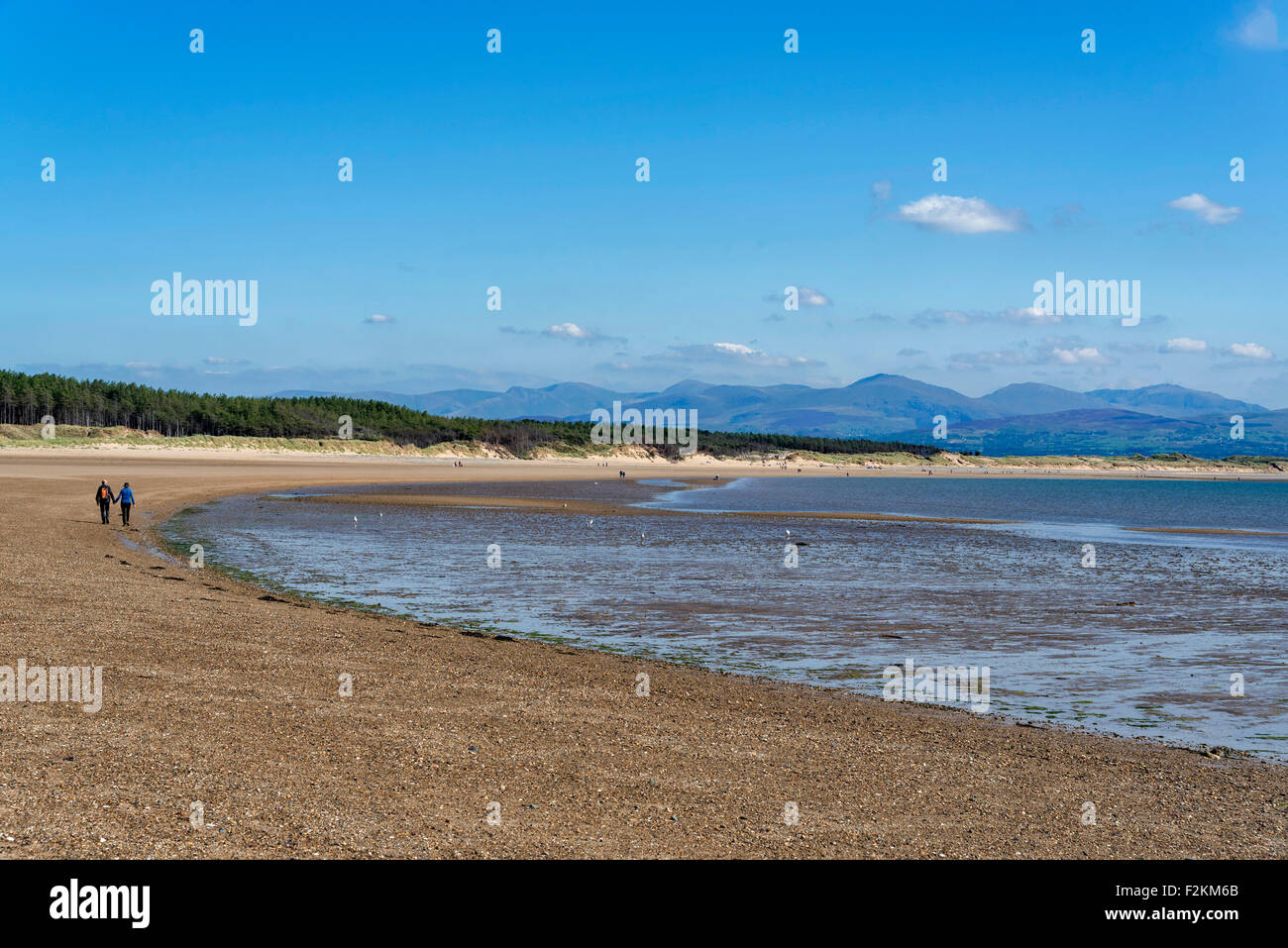 La plage de la baie de Llanddwyn. Anglesey au nord du Pays de Galles. Couple en train de marcher. Montagnes de Snowdonia en arrière-plan. Banque D'Images
