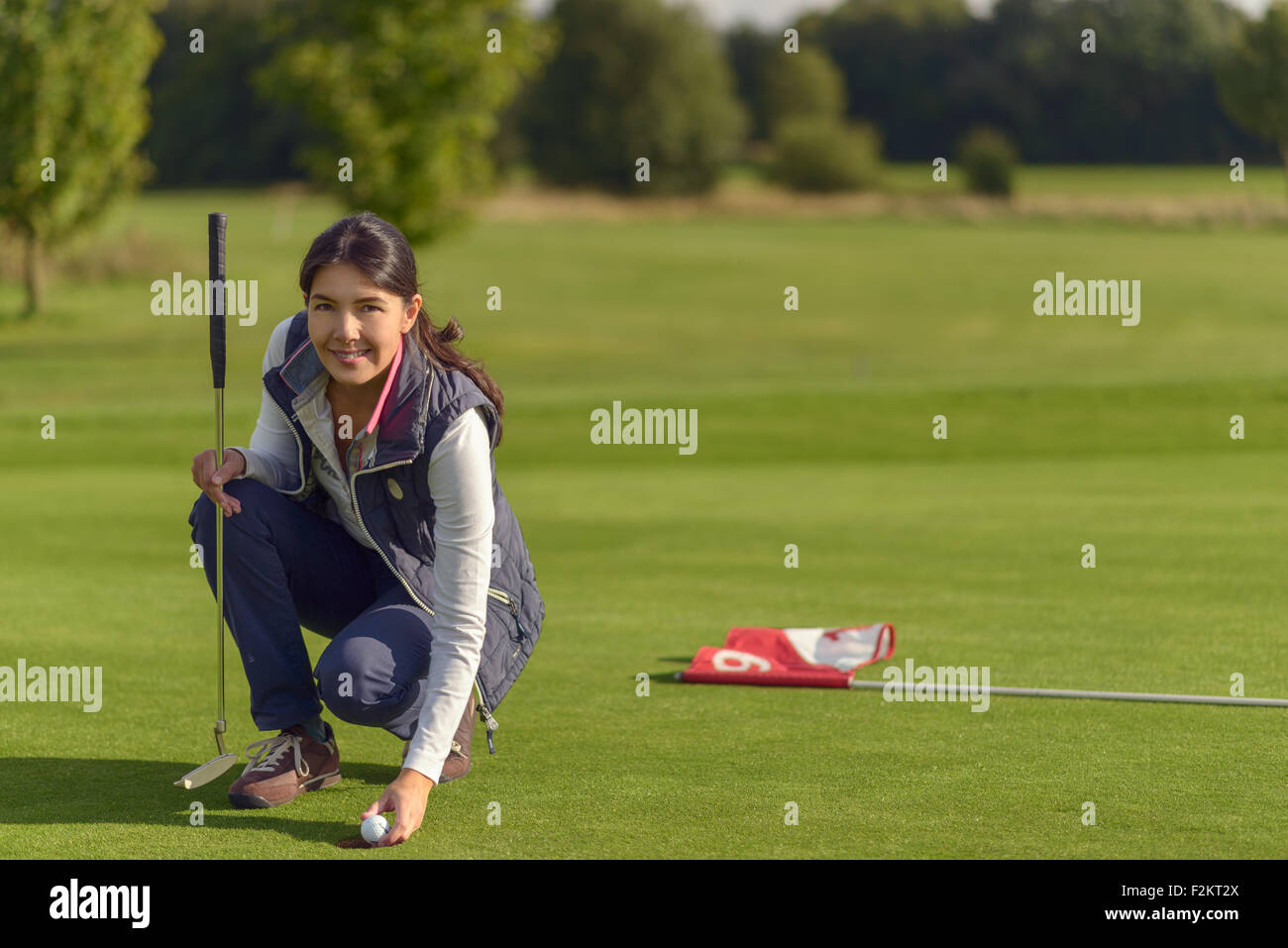Golfeuse attrayant de ramasser une balle de golf du trou après avoir fait un bon score, smiling at the camera Banque D'Images