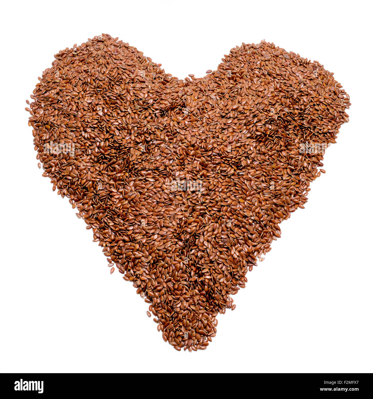 Un tas de graines de lin brun formant un coeur sur fond blanc Banque D'Images
