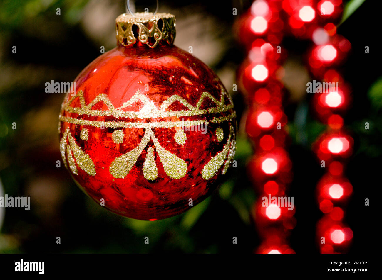 Close up detail d'une boule de noël rouge vif avec décoration dorée en face d'une même luminosité chaîne de perles rouges Banque D'Images