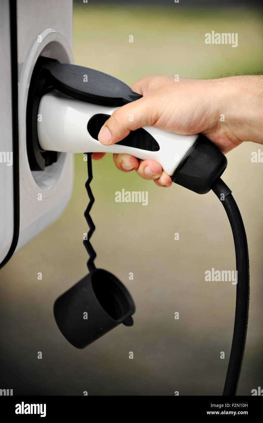 Main tenant une prise électrique pour recharger en voiture électrique Banque D'Images