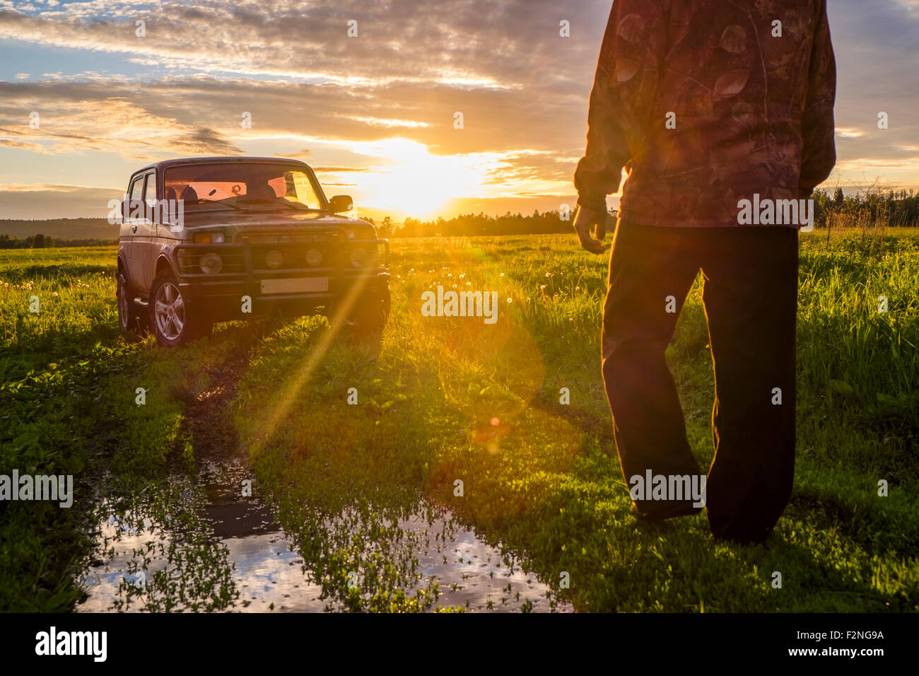 Mari homme à marcher en direction de voiture à Sunset in rural field Banque D'Images