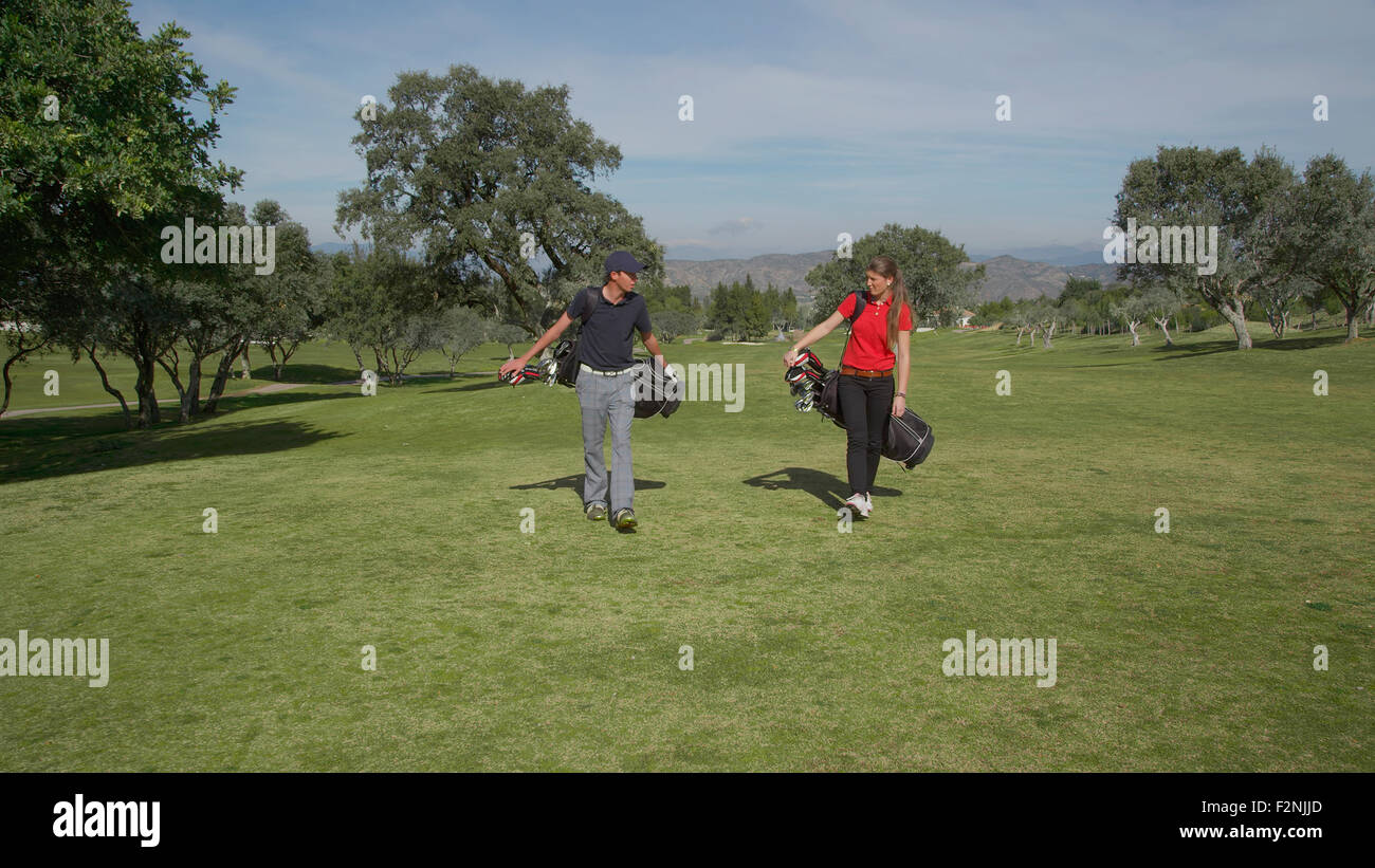 Caucasian couple transportant des sacs de golf on course Banque D'Images