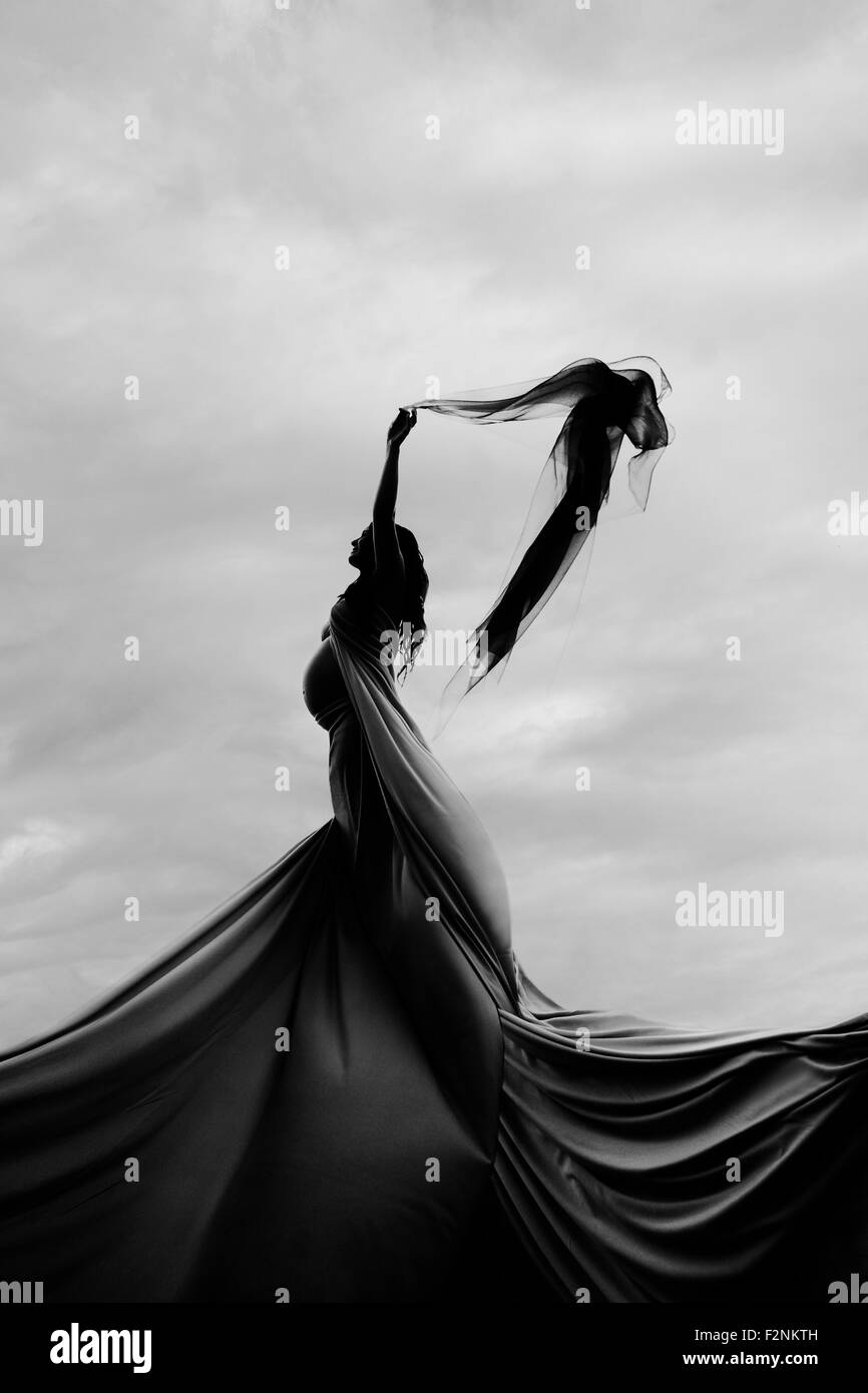 Caucasian woman twirling en tissu sous les nuages Banque D'Images