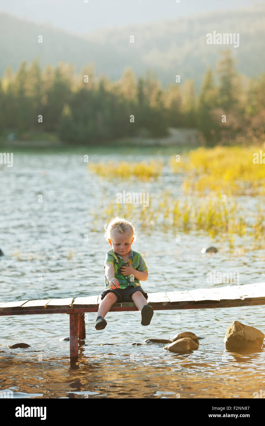 Young boy sitting on deck en bois sur le lac Banque D'Images