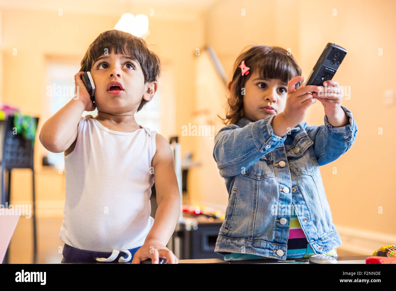 Frère et sœur jouant avec téléphone cellulaire et commande à distance Banque D'Images