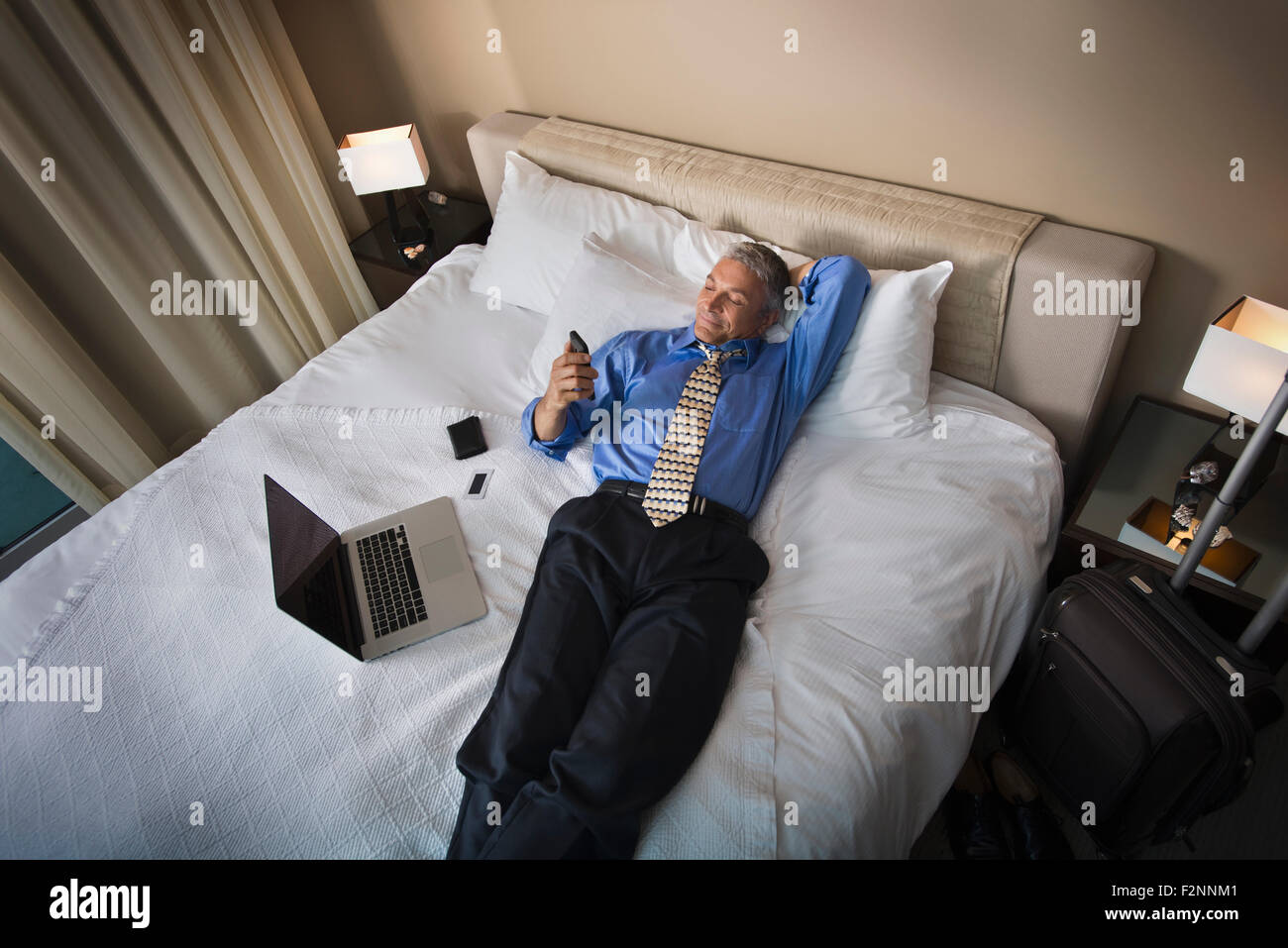 Caucasian businessman using cell phone on hotel bed Banque D'Images