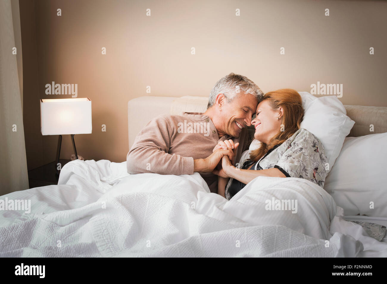 Smiling couple holding hands on bed Banque D'Images