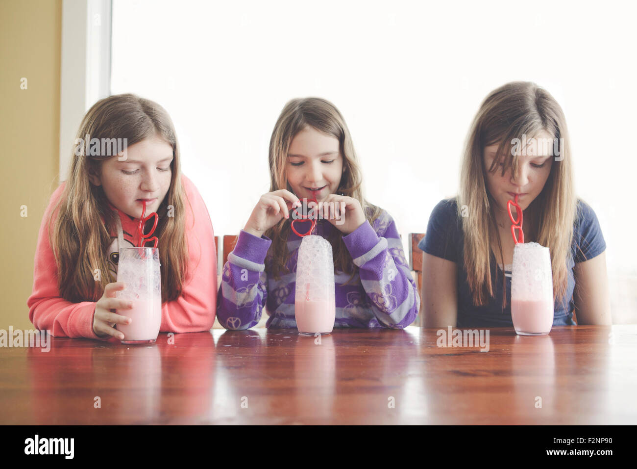 Filles caucasiennes boire du lait avec une paille enroulée à table Banque D'Images