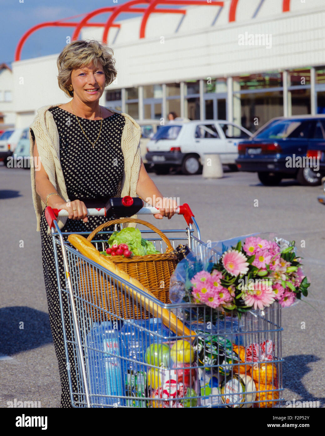 Smiling mature woman with shopping trolley au supermarché Banque D'Images