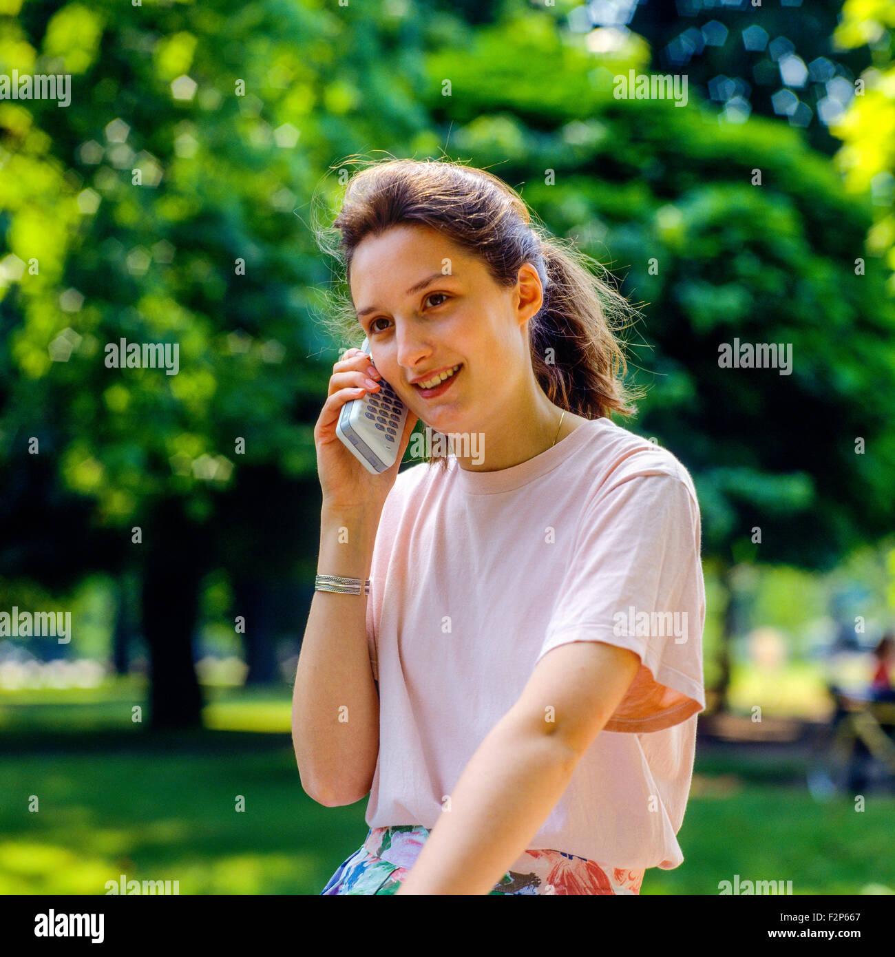 Adolescente souriante parlant sur son téléphone cellulaire à Park, France, Europe Banque D'Images