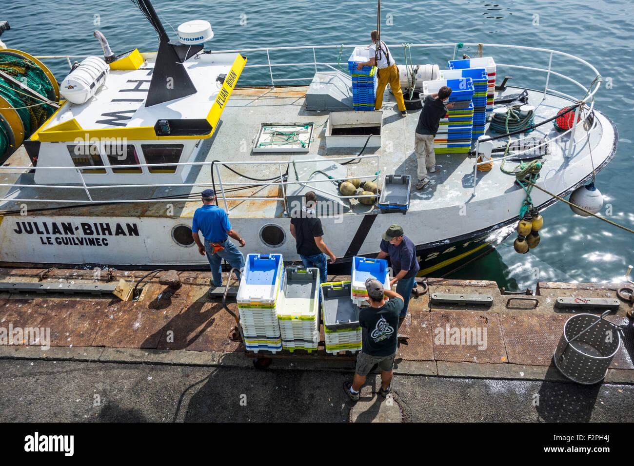 Les pêcheurs à bord du bateau de pêche le chargement des bacs en plastique le long de quai de marché aux enchères du poisson dans le port du Guilvinec, Bretagne, France Banque D'Images