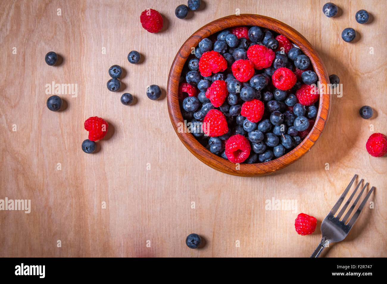 Les bleuets et les framboises dans un bol en bois sur fond sombre Banque D'Images