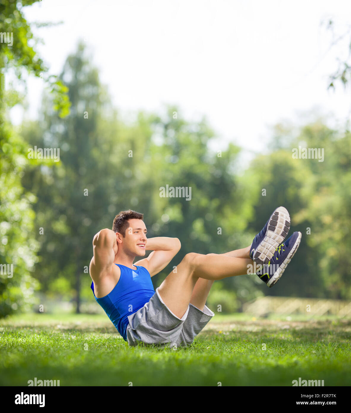 Jeune athlète faisant reposer-se lève avec les jambes dans un parc sur une belle journée d'action avec l'objectif de décentrement et Banque D'Images