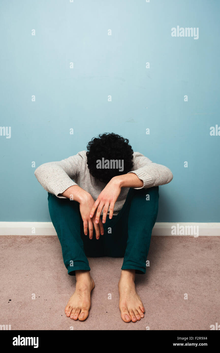 Un jeune homme triste dans assis sur le sol contre un mur bleu Banque D'Images