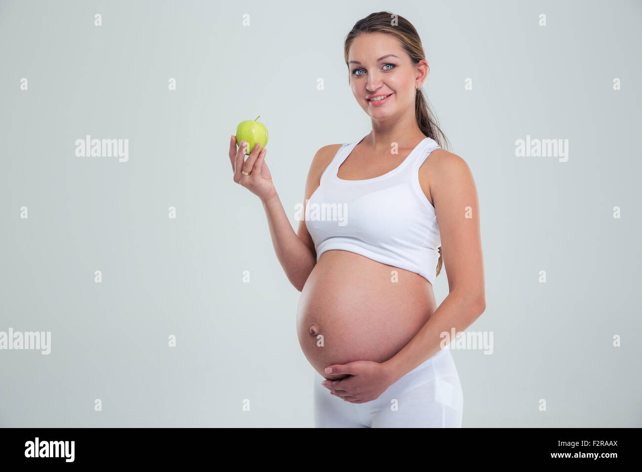 Portrait of a happy pregnant woman holding apple isolé sur un fond blanc, looking at camera Banque D'Images