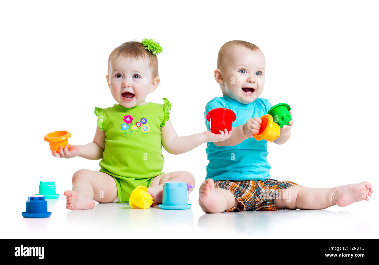 Adorable bébé jouant avec des jouets de couleur. Enfants fille et garçon assis sur le sol. Isolé sur fond blanc. Banque D'Images