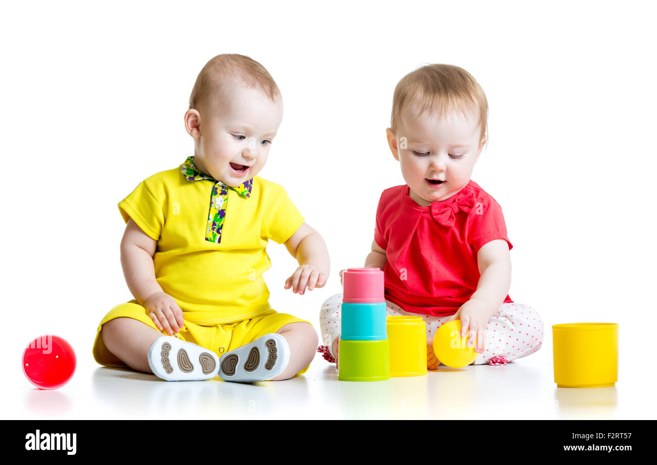 Cute kids jouant avec des jouets de couleur. Enfants fille et garçon assis sur le sol. Isolé sur fond blanc. Banque D'Images