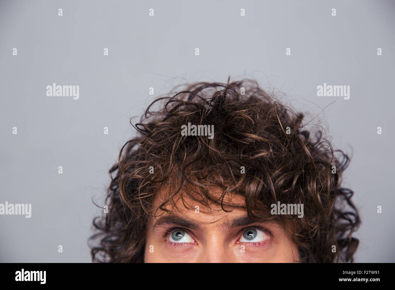 Portrait d'un homme avec les cheveux bouclés à la recherche jusqu'à copyspace sur fond gris Banque D'Images