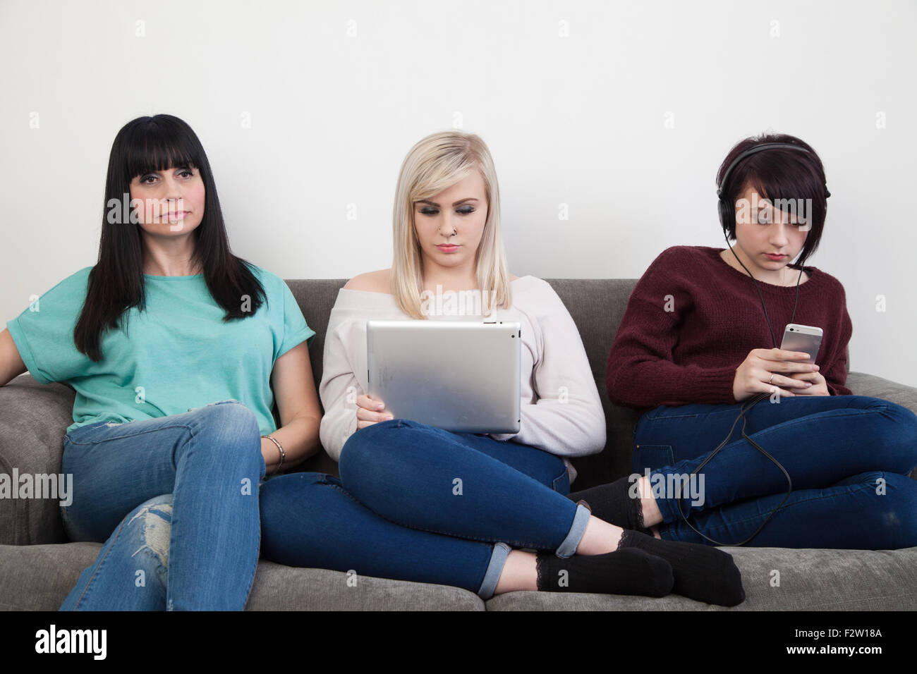 Mère et ses deux filles assise sur un canapé en regardant la télé , à l'aide d'un ipad et d'écouter de la musique. Banque D'Images