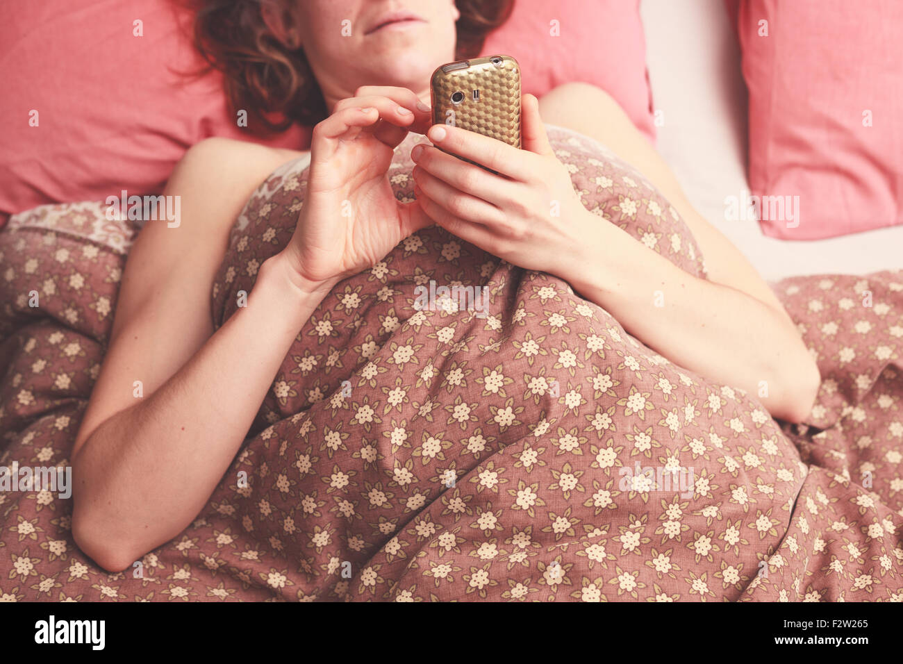 Jeune femme est au lit et l'envoi d'un texte sur son téléphone Banque D'Images