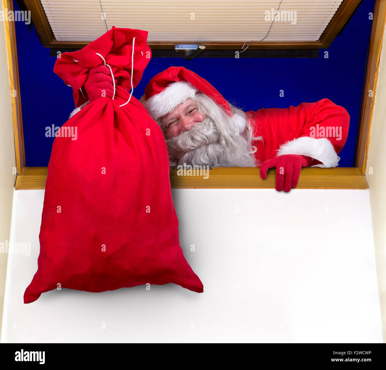 Père Noël transportant un sac de cadeaux et monte dans la chambre par la fenêtre Banque D'Images