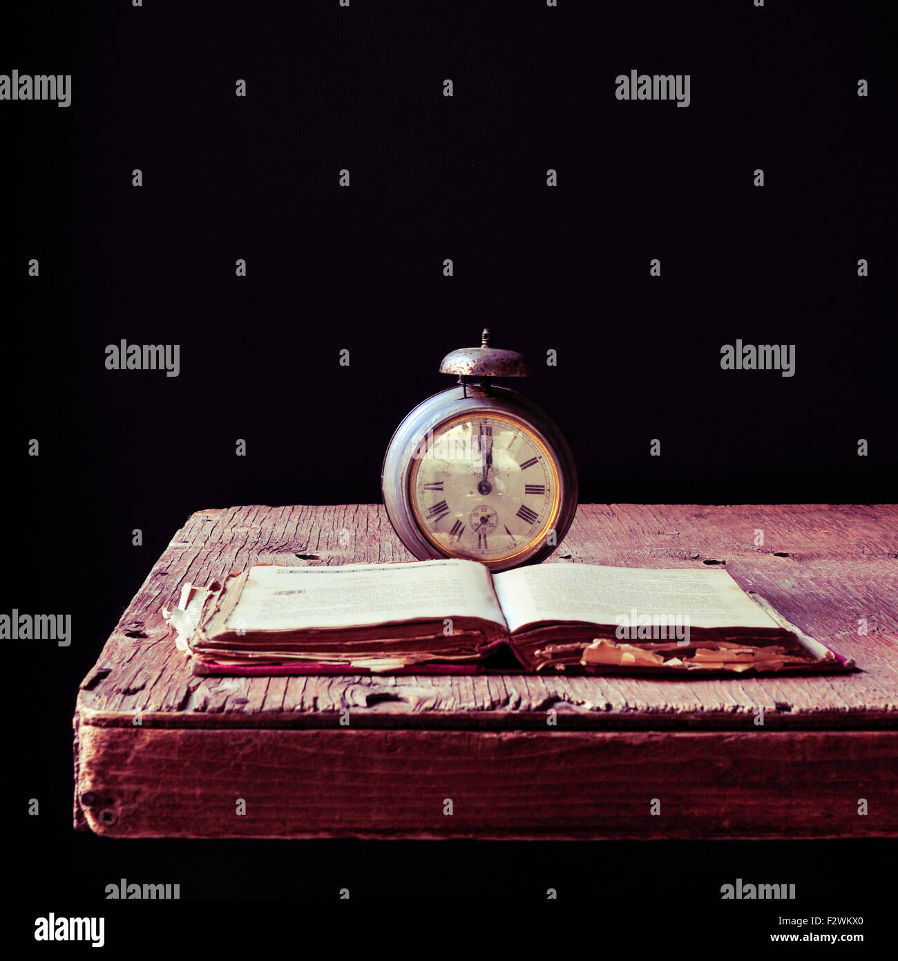 Un vieux réveil et un vieux livre ouvert sur une table en bois rustique, d'un fond noir Banque D'Images