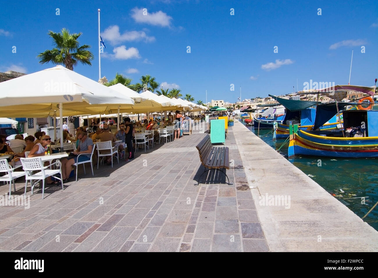 Le restaurant Pier Marsaxlokk avec parasols, bateaux colorés et des signes sur une journée ensoleillée, à Malte. Banque D'Images