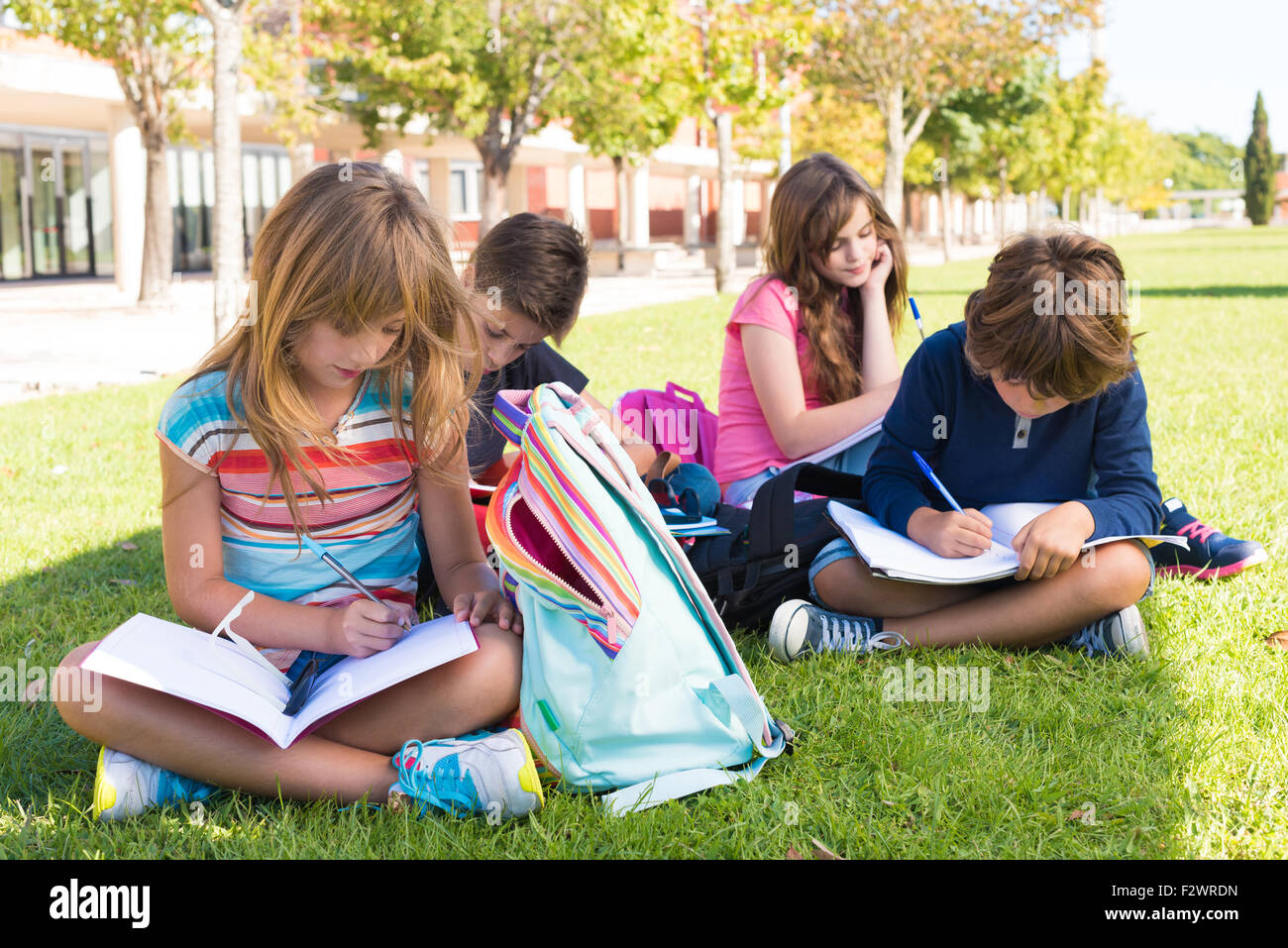 Groupe de petits étudiants assis sur l'herbe à l'école Banque D'Images