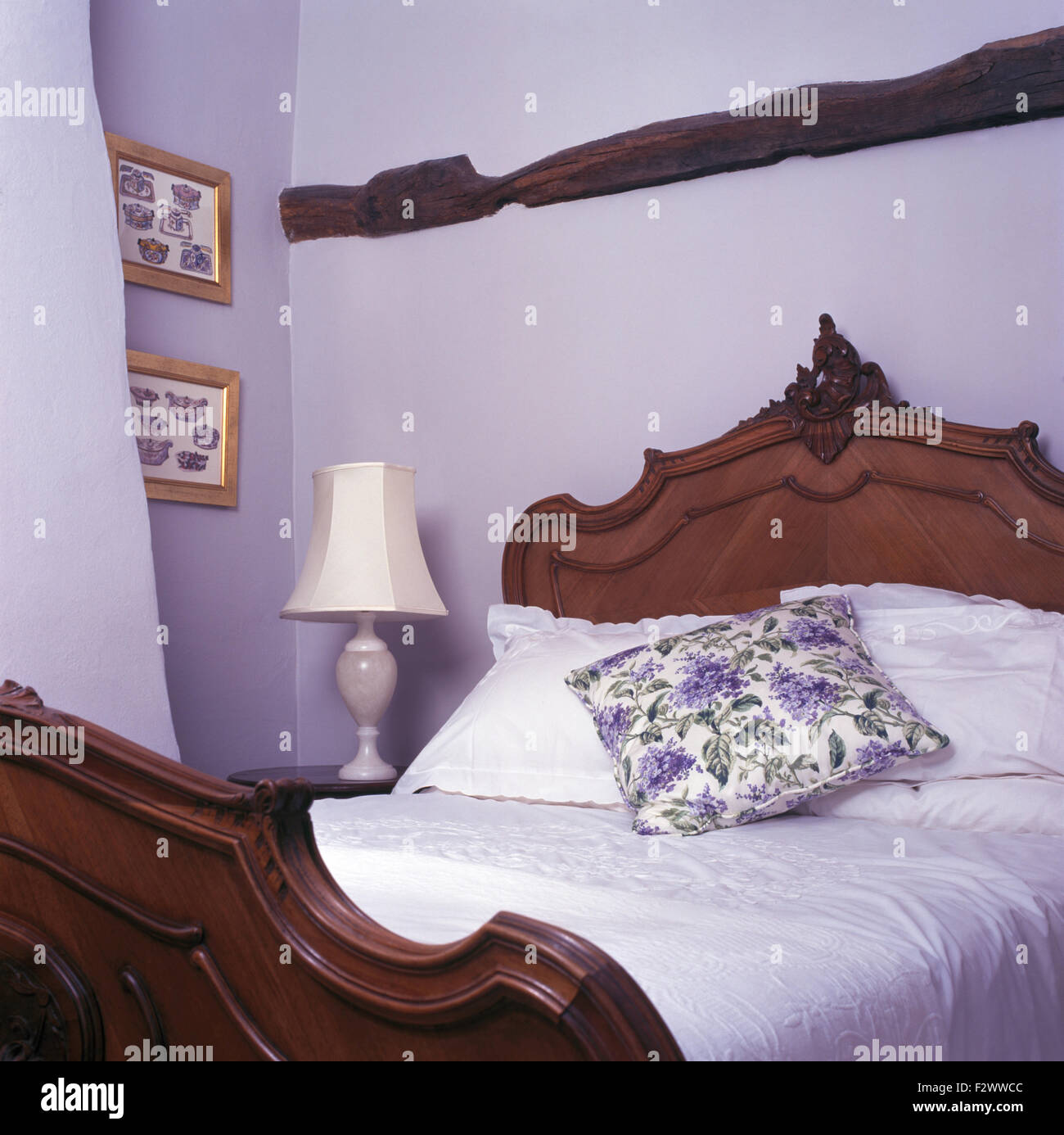 Chambre Cottage avec lampe à côté de lit en bois sculpté avec un coussin de fleurs mauve et blanc en coton Banque D'Images