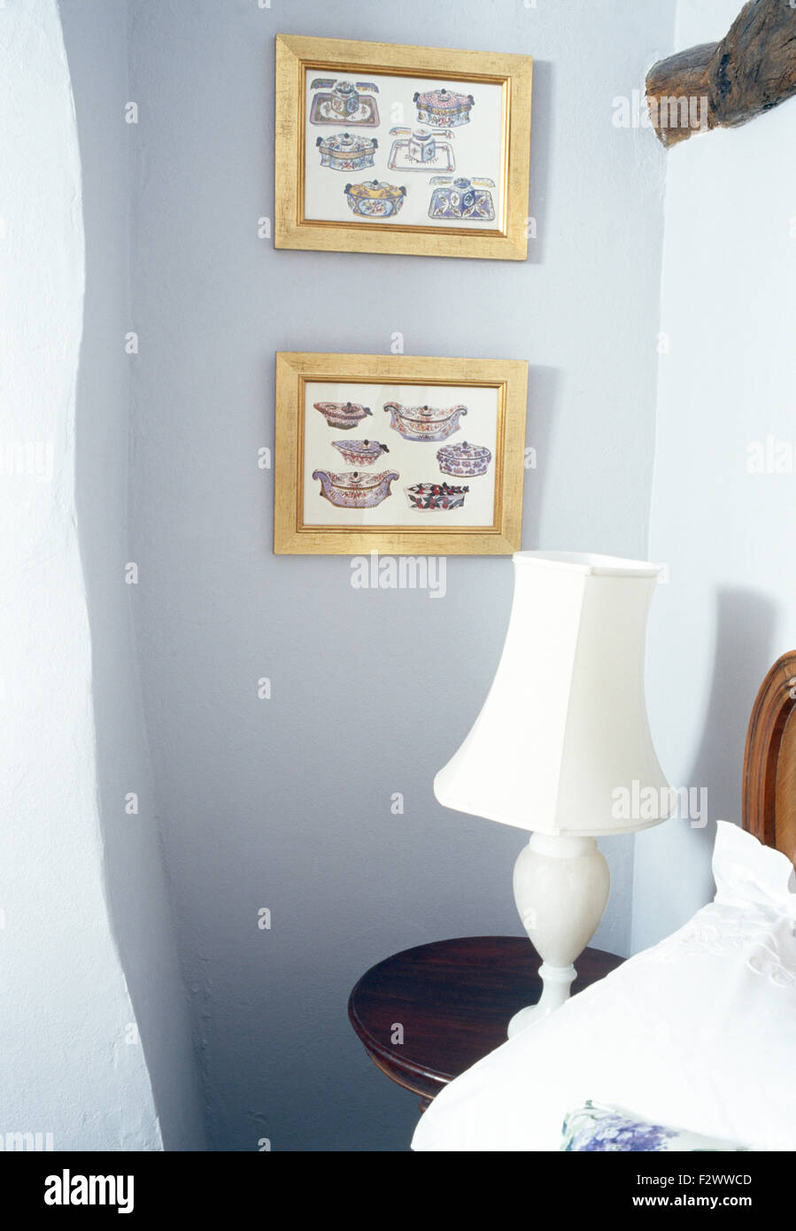 Le GILT gravures encadrées sur le mur au-dessus de table de chevet avec lampe blanche en chambre cottage Banque D'Images