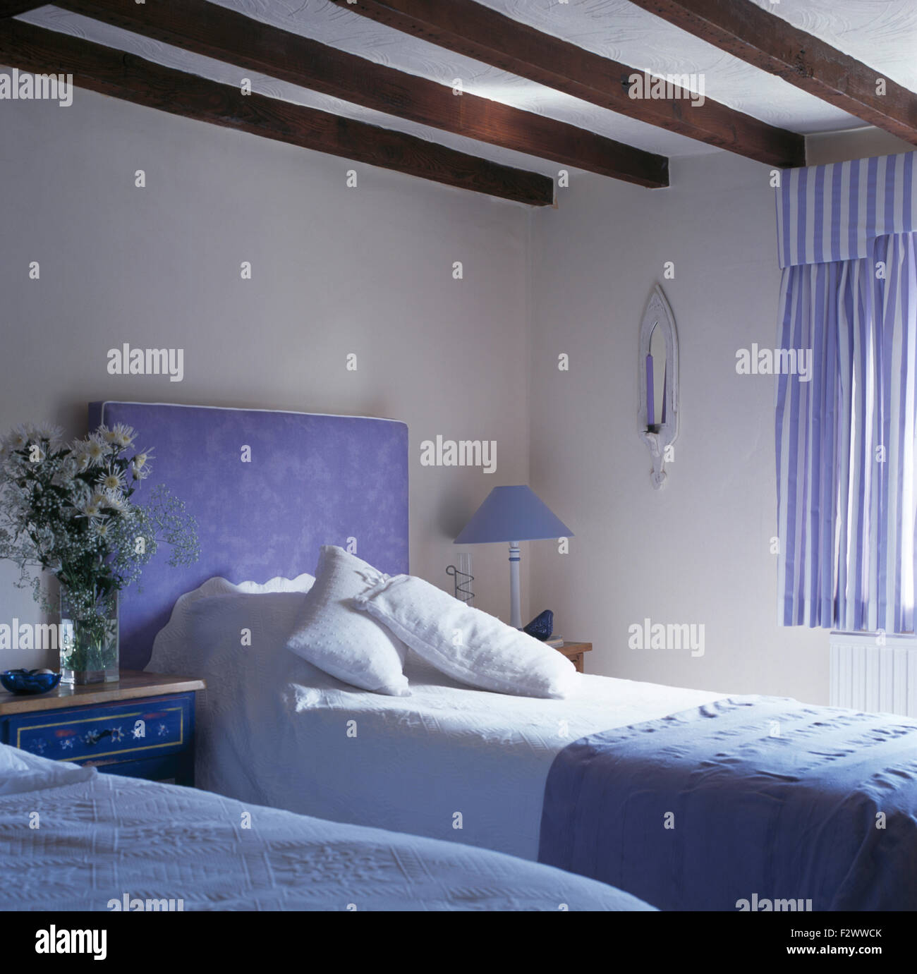 Tête de lit bleu rembourré sur lit avec draps blancs en pays chambre avec des rideaux à rayures blanc +bleu Banque D'Images