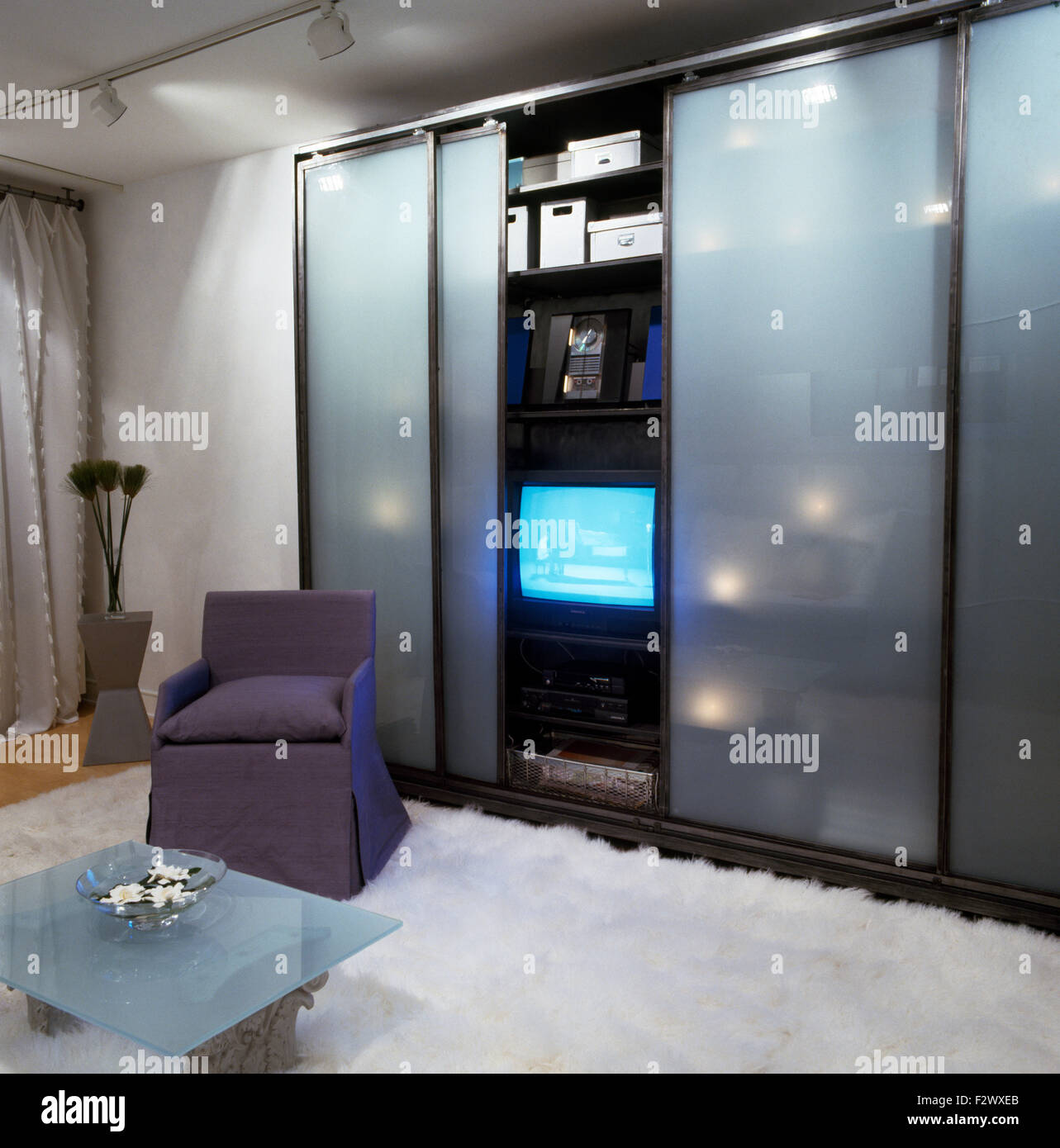 Portes coulissantes en verre opaque sur armoire avec télévision dans ville chambre avec tapis de fourrure blanche sur le sol Banque D'Images