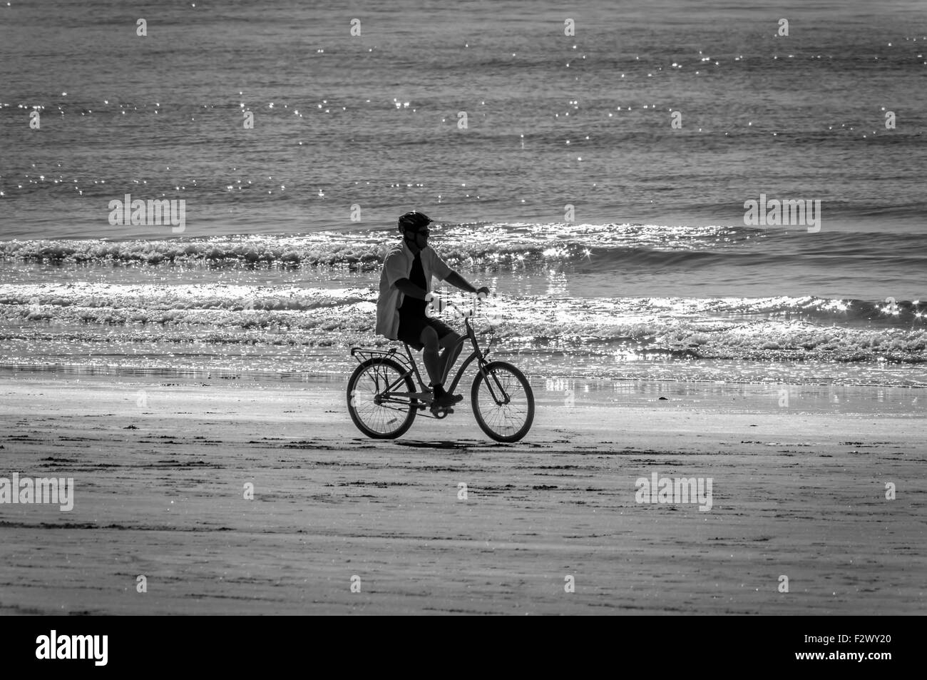 Sur un très tôt le matin, avant que la foule arrive à la plage, ce que l'homme prend un tour sur son vélo tout seul sur le sable humide. Banque D'Images