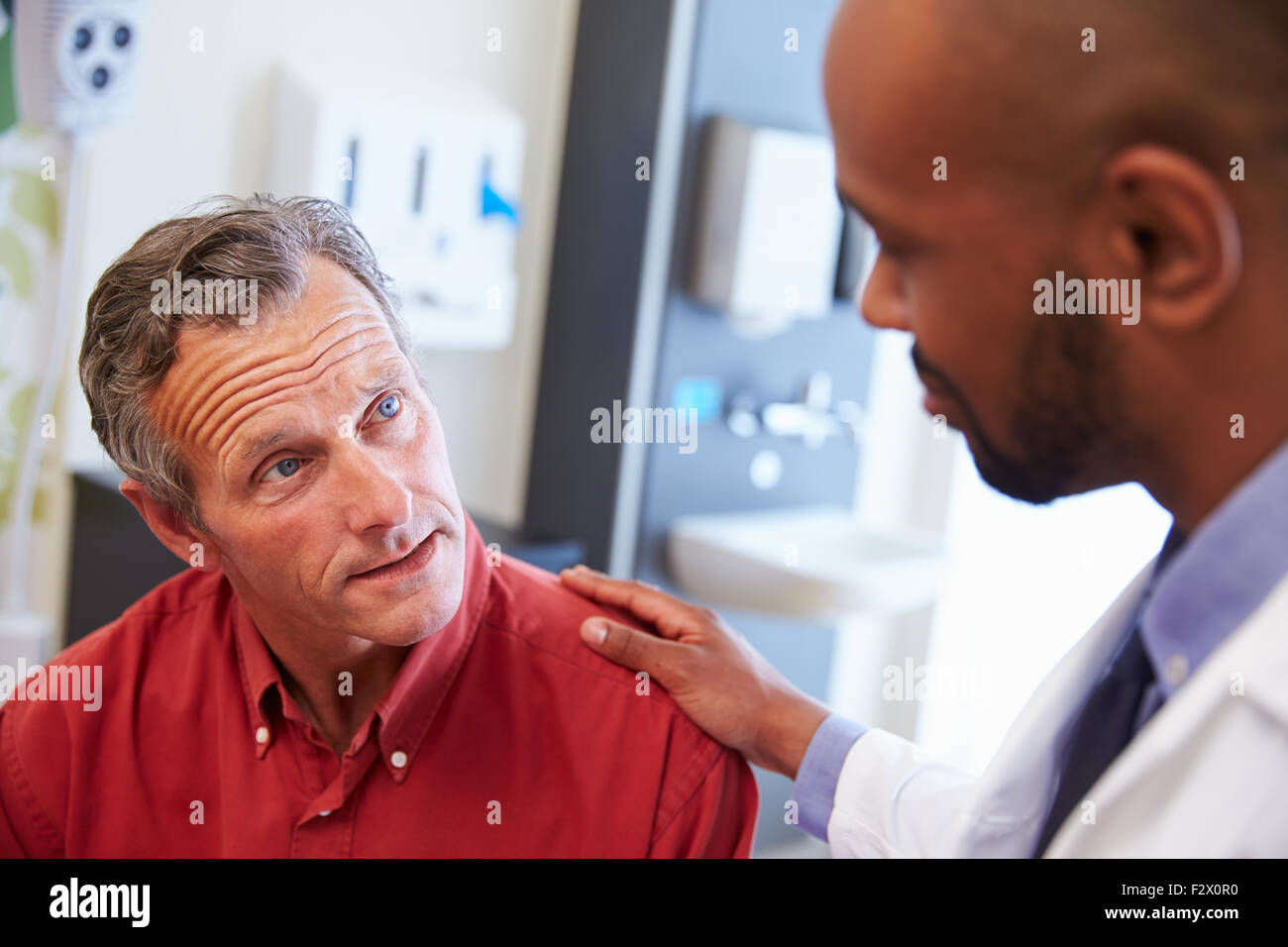 Patient de sexe masculin d'être rassuré par Doctor in Hospital Room Banque D'Images